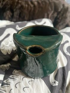 a green vase sitting on top of a bed next to a black and white blanket