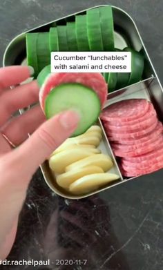 a person is holding a pickle in a container with sliced vegetables and meats