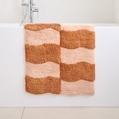 two bath mats sitting next to each other on a white wall near a tub and faucet