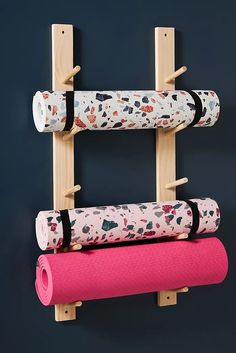 three yoga mats are hanging on the wall next to a wooden rack with two handles