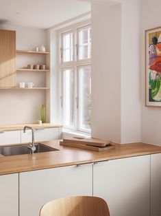 a kitchen with white walls and wooden cabinets, an island countertop and a painting on the wall