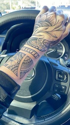 a person with a tattoo on their arm driving a car and holding the steering wheel