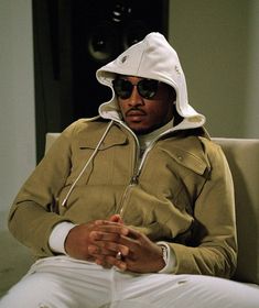 a man sitting on top of a couch wearing a white hat and jacket with his hands in his pockets