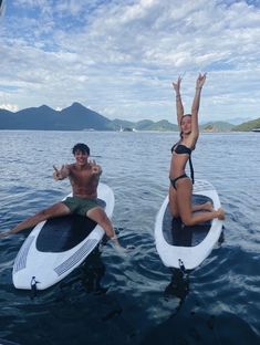 two people on surfboards in the water with their arms up and one person sitting on top