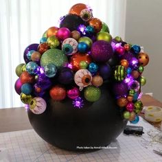 a vase filled with lots of colorful ornaments on top of a wooden table next to a window