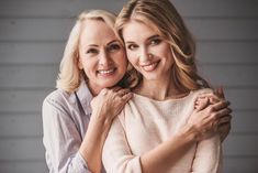 two women are hugging each other in front of a wall and one is wearing a sweater