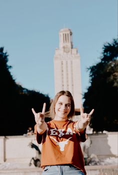 a woman standing in front of a tall building making the peace sign with her hands