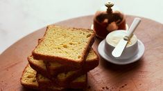 two slices of bread on a wooden plate next to a tea pot and spoons