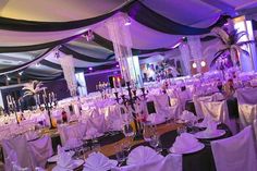 a banquet hall set up with white linens and purple lighting, decorated for an event