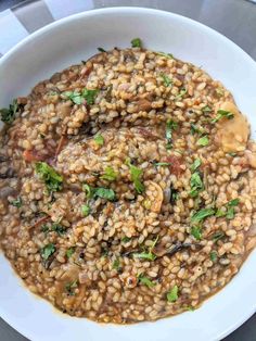 a white bowl filled with brown rice and vegetables on top of a table next to a fork