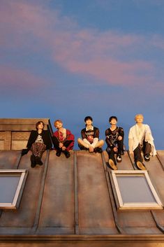 five people sitting on top of a building with windows and sky in the back ground