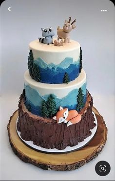 a three tiered cake decorated with animals and trees on it's sides, sitting on top of a tree stump