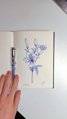 a hand is holding a pen over an open notebook with blue ink on it, and there are flowers in the pages