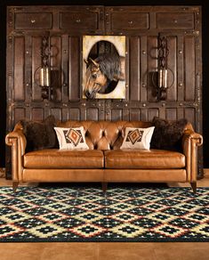 a brown leather couch sitting in front of a wooden wall with two horses on it