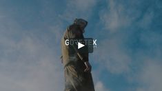 a man standing on top of a tall statue under a blue sky filled with clouds