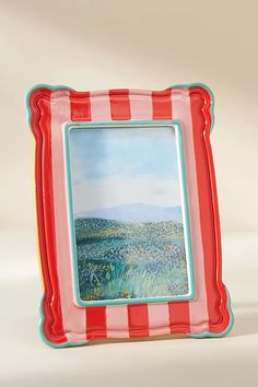 a red and white striped frame with a painting on the front is holding an image of a field