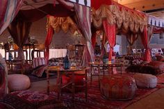 an elaborately decorated room with red and gold drapes on the ceiling, round tables in between two couches