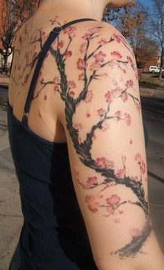 a woman with a tattoo on her arm is walking down the street in front of a tree