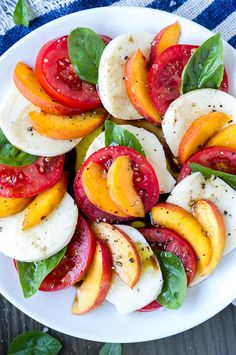 a white plate topped with sliced peaches and mozzarella on top of spinach leaves