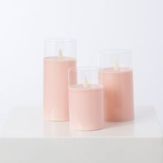 three pink candles sitting on top of a white table next to each other in front of a white wall