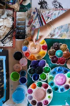 someone is painting with their hands on some paint bowls and brushes in front of them