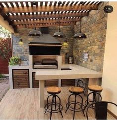 an outdoor kitchen with bar stools next to the stove and counter top, in front of a stone wall