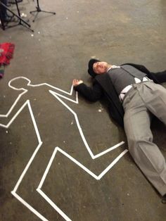 a man laying on the ground in front of a chalk drawing of a man's body