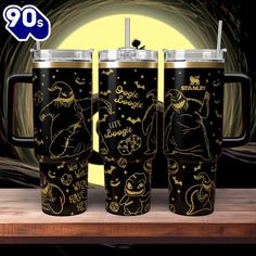 three black and gold mugs with the same design on them, sitting on a wooden table