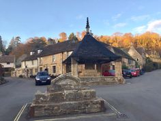 an old stone building with a black roof in the middle of a road surrounded by parked cars