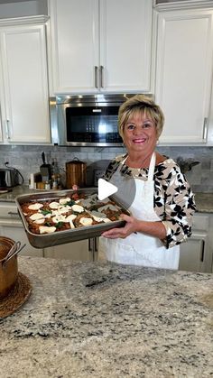 a woman holding a pan with food on it in a kitchen next to an oven