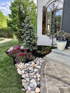 a house with flowers and rocks in the front yard, along with a tree on the side