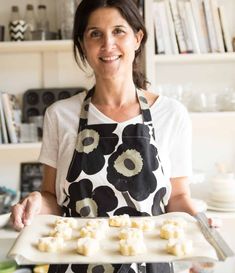 a woman in an apron holding a tray with food on it and smiling at the camera