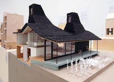 an architectural model of a house on display in a room with white walls and black roof