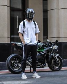 a man in white shirt and black pants standing next to motorcycle