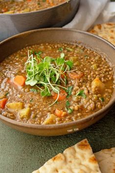 a bowl of lentula soup with pita bread and garnish on the side