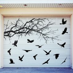 a group of birds flying in front of a garage door with a tree branch on it