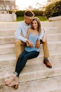 a man and woman sitting on the steps together in front of some stairs with their arms around each other