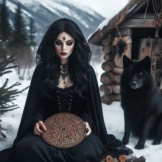 a woman sitting in the snow next to a black dog and holding a wooden plate