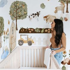 a woman standing next to a baby crib in front of a wall with farm animals on it