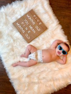 a baby wearing sunglasses laying on top of a fluffy white rug next to a book