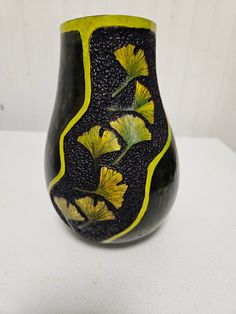 a black vase with yellow flowers painted on the outside and inside, sitting on a white surface