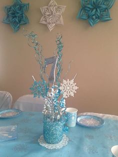 a centerpiece with snowflakes and other decorations on a blue table cloth covered table