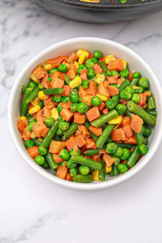 a bowl filled with peas and carrots next to a skillet full of vegetables