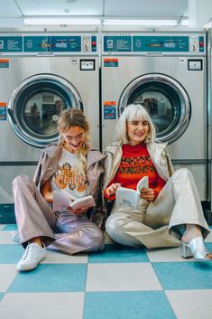 two women sitting next to each other in front of washers and dryer machines