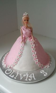 a barbie doll cake with pink and white frosting on the top, sitting on a silver platter