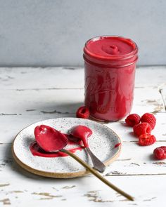 raspberry sauce in a jar and spoon on a plate with raspberries