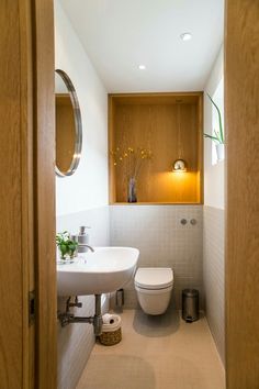 a white toilet sitting next to a sink in a bathroom under a mirror and light