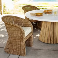 two wicker chairs and a round table with plates on it, sitting in front of a pool