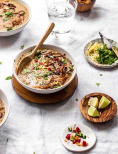 several bowls of food on a table with plates and spoons next to them,