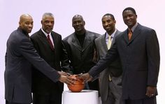 four men in suits are holding a basketball and shaking it with each other's hands